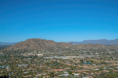 Phoenix, Arizona 'daki Camelback Dağı' ndaki yürüyüş parkurundan bir kasaba manzarası. Dağların yakınındaki binaların ve yolların mavi gökyüzü arka planına bakan görüntüsü.