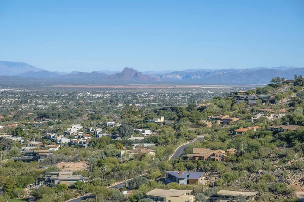 View of suburban residence from Camelback Mountain hiking trail at Phoenix, Arizona. High angle view of a sloped residential area with large residential buildings and view of mountains at the back.