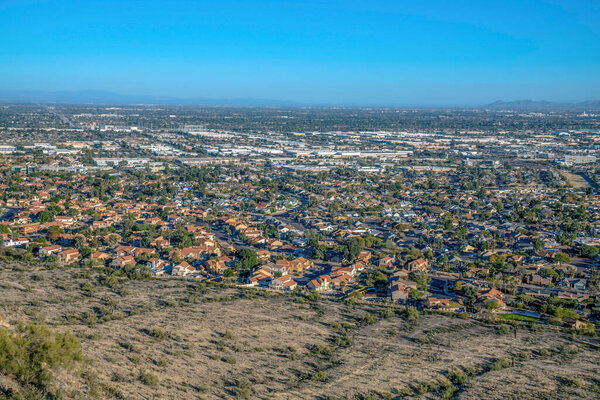 Phoenix, Arizona- View of wealthy neighborhood below the Pima Canyon trail. There is a residential area near the mountain slope at the front and a view of commercial buildings at the back.