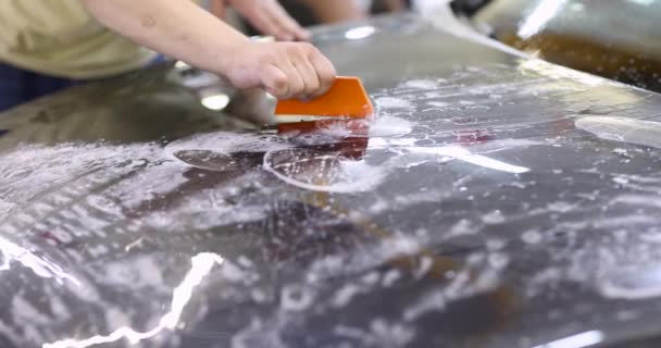 Reparaturmeister klebt schützende Vinylfolie auf Motorhaube des Autos in Garage 4k Film — Stockvideo