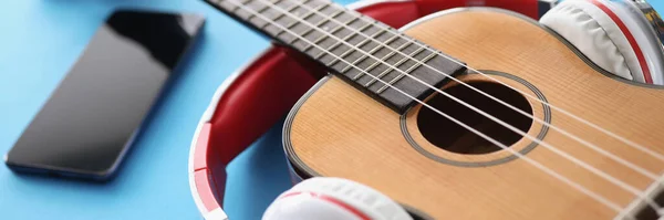 Wooden guitar headphones. and smartphone on blue background