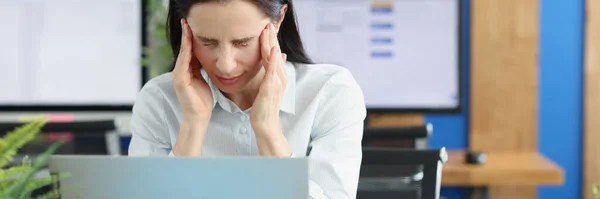 Mujer joven con dolor de cabeza detrás del ordenador portátil en el lugar de trabajo — Foto de Stock