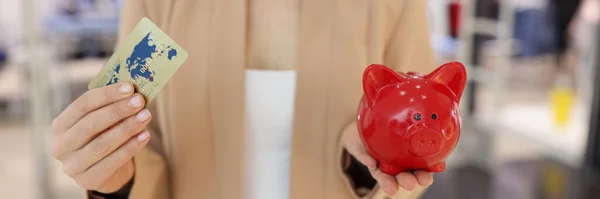 Zakenvrouw houdt in haar hand krediet plastic bankkaart en rode varken spaarpot — Stockfoto