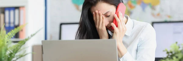 Mujer joven molesta hablando en el teléfono inteligente mientras está sentado en el lugar de trabajo — Foto de Stock