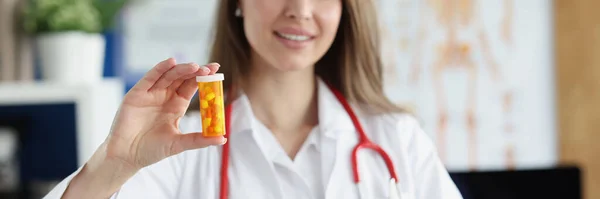 Smiling family medicine doctor holds and gives patient jar of pills