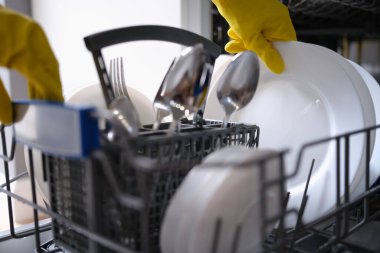 Sarı eldivenli biri bulaşık makinesinden temiz tabakları çıkarır.
