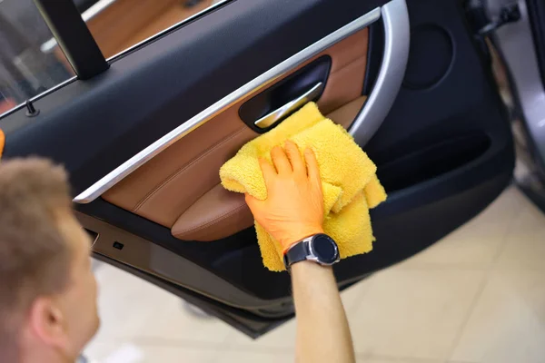 Male washer in gloves wipes car door with microfiber closeup