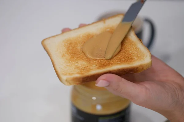 Женщина разбрасывает арахисовое масло на тосте с ножом крупным планом — стоковое фото