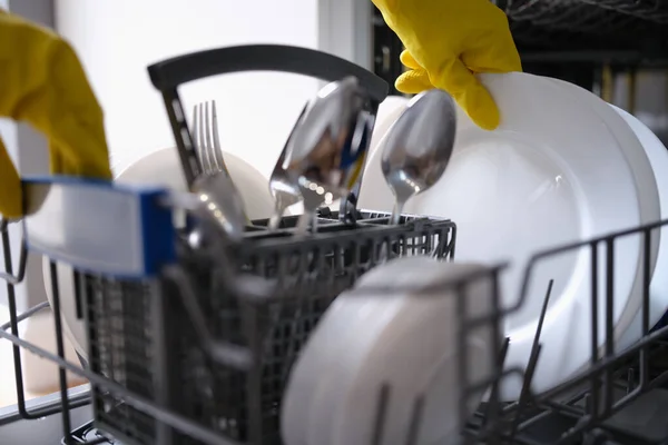 Person in yellow gloves takes clean dishes out of dishwasher