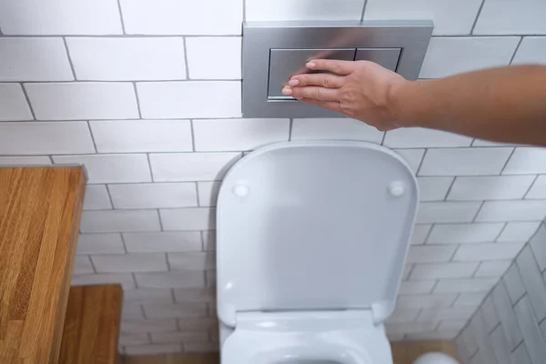 Женщина нажимает кнопку смыва в туалете крупным планом — стоковое фото
