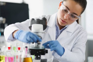 Koruyucu gözlüklü kadın kimyager laboratuvarda cam sürgü takıyor.