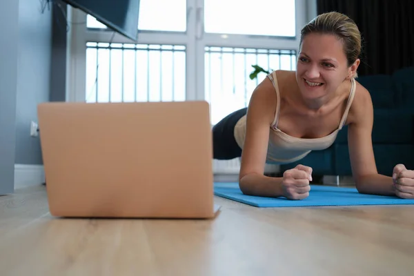 Young woman standing in plank on floor in front of laptop — Stock Photo, Image