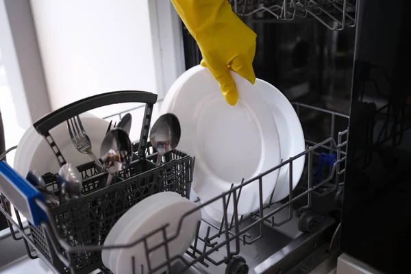 Mano femenina en guante de goma poniendo platos sucios en primer plano lavavajillas — Foto de Stock