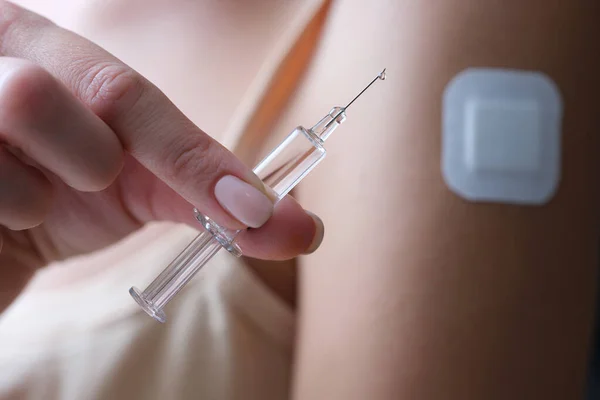 Woman holding syringe with vaccine in her hands near shoulder with plaster closeup