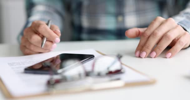 Femme assise à table avec des documents et un téléphone portable et se cogner les doigts sur la table film 4k — Video