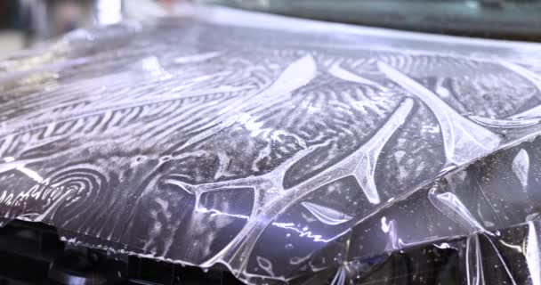 Мастер-ремонтник упаковки виниловой полиуретановой пленки на капоте автомобиля в мастерской 4k кино — стоковое видео