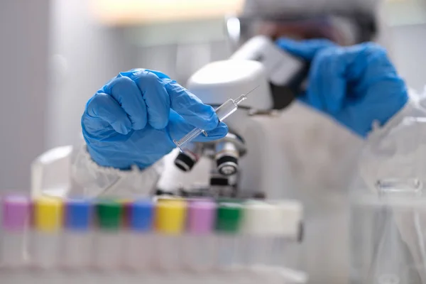 Ученый-химик в защитном костюме смотрит через микроскоп в лабораторном макро — стоковое фото
