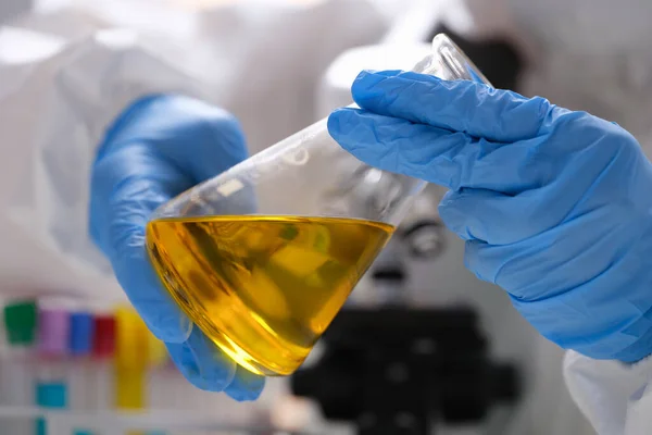 Científico químico en guantes de goma protectora sosteniendo matraz con primer plano líquido amarillo — Foto de Stock