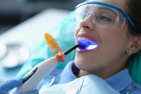 Dentysta stosujący ultrafioletowe narzędzie do utwardzania zębów podczas zabiegu z pacjentem w klinice — Zdjęcie stockowe