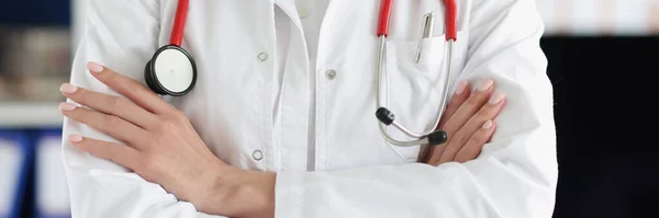Mujer doctora con estetoscopio rojo de pie en uniforme con las manos dobladas de cerca —  Fotos de Stock
