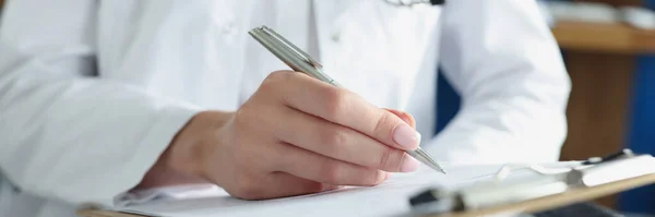 Doctor writing in medical documents on clipboard in clinic closeup