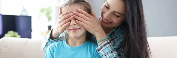 Mother covering her daughter eyes with her hands. Little girl holding box with gift — Stock Photo, Image