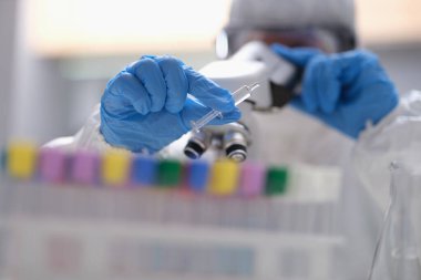 Bilim adamı cam şırıngaya iğneyle mikroskopla bakıyor.