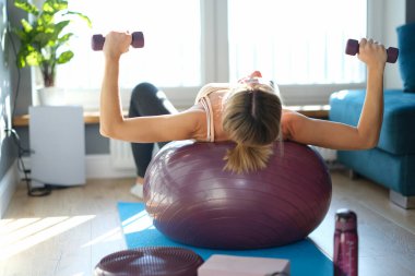 Topun üzerinde yatan genç kadın dambılları yakın çekimde kaldırır.