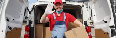 Yakışıklı kurye, karton kutuyu minibüsten çıkarıp el sallıyor.
