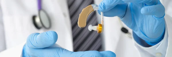 Оториноларинголог держит слуховой аппарат с резиновыми перчатками крупным планом — стоковое фото