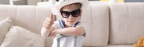 Menina em chapéu e óculos de sol fica com mala e segura os polegares para cima — Fotografia de Stock