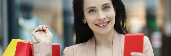 Portret van een jonge glimlachende vrouw met smartphone en pakketten met aankopen — Stockfoto