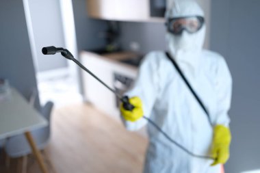 Koruyucu elbise giyen ve maske takan kişi mutfağı dezenfekte eder.