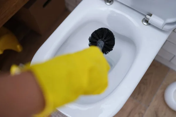 Mão na luva está limpando vaso sanitário com escova preta close-up — Fotografia de Stock