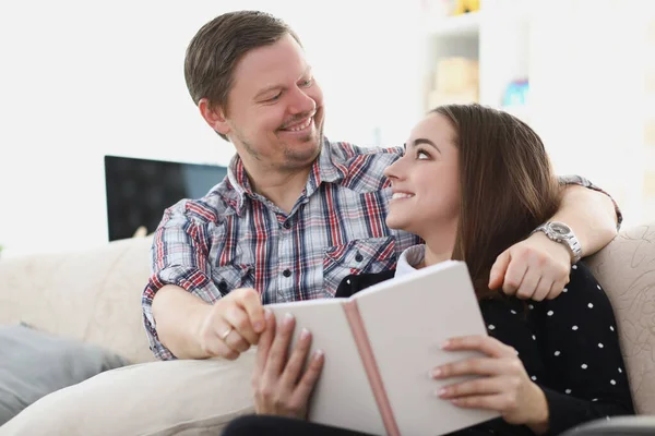 Unga gifta par sitter på soffan med bok och tittar på varandra — Stockfoto