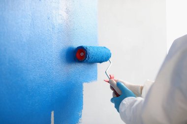 Tamirci, mavi dairedeki beyaz duvarı paten kullanarak boyuyor.