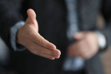 Takım elbiseli bir işadamı, ortağının elini sıkmak için elini uzatıyor.