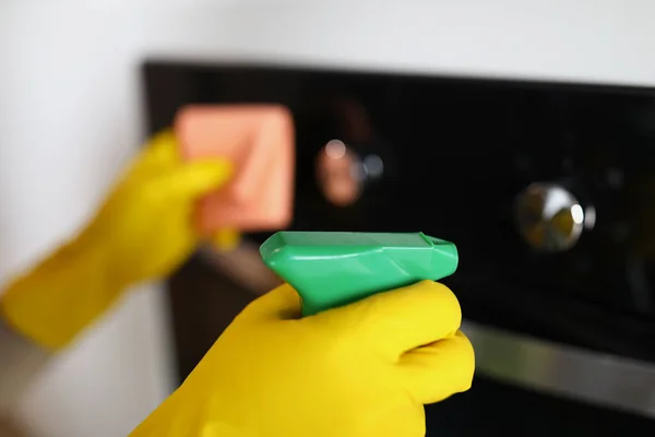Huisvrouw in geel rubber handschoenen puffen spray van chemische reiniger op kachel closeup — Stockfoto