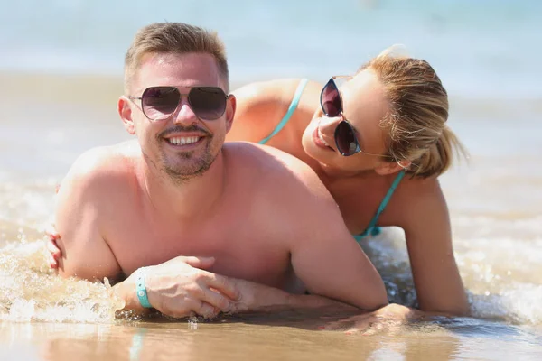 Giovane felice uomo e donna in occhiali da sole sdraiato sulla riva del mare — Foto Stock