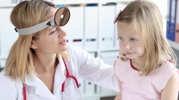 Лікар-оторхіноларинголог з фронтальним рефлектором вивчає вухо маленької дівчинки з аутоскопом 4k плівки — стокове відео