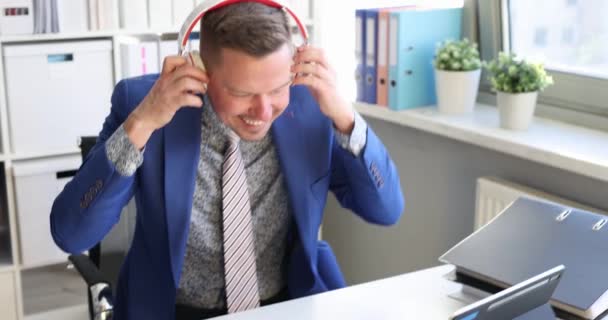 Jongeman in zakenpak zet een koptelefoon op en danst in kantoor 4k film — Stockvideo