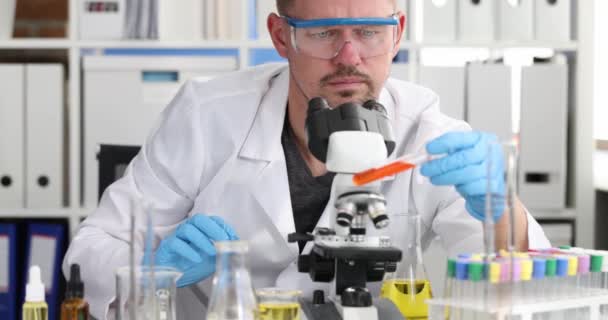 Scientist chemist wearing glasses holding test tube with blood and looking microscope 4k movie — Stock Video