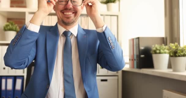 Joven hombre de negocios sonriente en traje sentado en la mesa y poniendo gafas para la visión 4k película — Vídeo de stock