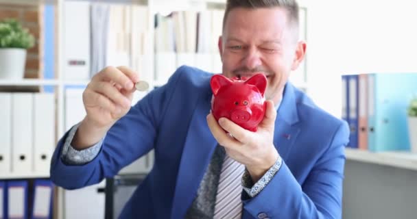 Takım elbiseli genç adam Red Piggy Bank 4K filmine bozuk para atıyor. — Stok video