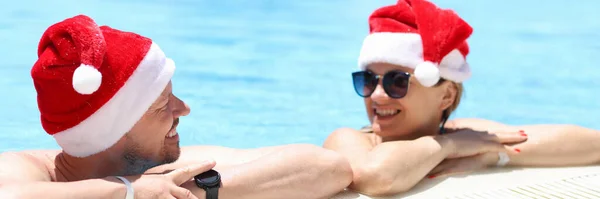 Jovem e mulher de óculos de sol e chapéus de Papai Noel falando na piscina — Fotografia de Stock