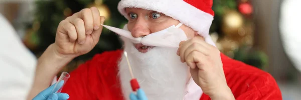 Doutor em luvas de borracha tomando toalhete nasal de pcr para Papai Noel perto da árvore de natal — Fotografia de Stock