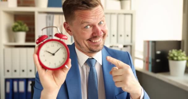 Retrato del gerente sonriente sosteniendo el despertador rojo para diez en la película de la mañana 4k — Vídeo de stock