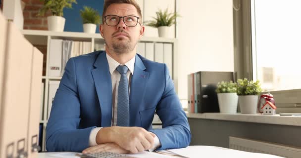 Jeune homme d'affaires dans des lunettes est assis judicieusement sur le lieu de travail et regarde par la fenêtre 4k film — Video