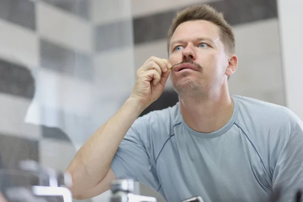 A man looks in the mirror and pulls his mustache — Stock Photo, Image