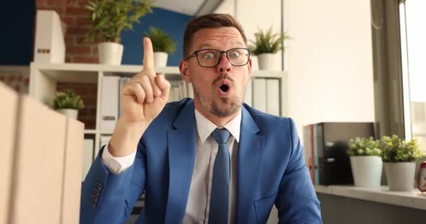 Удивленный бизнесмен сидит за столом и показывает указательный палец до 4k фильма — стоковое видео